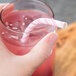 A hand holding a glass of pink liquid with a pink and white striped paper straw.
