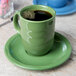 A green Libbey porcelain mug filled with a drink on a saucer.