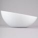 A Tablecraft white melamine bowl with a curved edge on a gray surface.