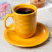 A yellow Libbey Cantina mug on a saucer with a black drink in it.