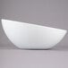 A Tablecraft Sierra white melamine bowl with a curved edge on a gray background.