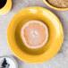 A close up of a Libbey porcelain grapefruit bowl with a slice of orange on a yellow plate.