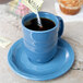 A hand pouring sugar from a bag into a blue Libbey porcelain mug.