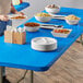 A blue rectangular table with white bowls and plates of food on it.