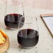 Two Acopa stemless wine glasses of wine next to cheese on a table.