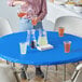 A woman pouring orange liquid into a plastic cup with a lid on a Royal Blue Stay Put tablecloth.