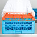 A chef holding a blue and orange Carlisle OptiClean glass rack extender.