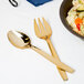 A Fineline heavy weight gold look serving spoon and fork next to a bowl of pasta.