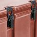 A close up of a Cambro brick red plastic soup carrier with two black latches.