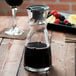 An Arcoroc glass carafe filled with red liquid on a table in a winery cellar.