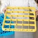 A person holding a yellow plastic tray with yellow dividers for glasses.