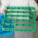 A person holding a green Carlisle glass rack extender on a green plastic tray.