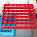 A person holding a red Carlisle glass rack extender with blue compartments.