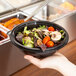 A person holding a black Fineline PET plastic bowl filled with salad at a salad bar.