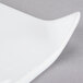 A close up of a Libbey white porcelain square plate with a curved edge and handle.