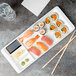 A Libbey porcelain 3-well tray with sushi and chopsticks on a table.