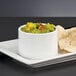 A Libbey ultra bright white porcelain canne bowl with guacamole and chips on a table.