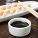 A Libbey white porcelain bowl filled with soy sauce next to sushi plates with chopsticks.