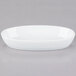 A close up of a Libbey ultra bright white porcelain oval bowl on a gray surface.