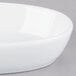 A close-up of a Libbey ultra bright white porcelain oval bowl on a gray surface.