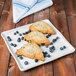 A close up of a blueberry scone on a Libbey Farmhouse ivory square tray with blueberries.