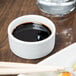 A Libbey ultra bright white porcelain bowl of soy sauce with chopsticks on a wood table.