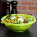 A green Fineline plastic bowl filled with salad on a table.