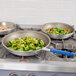 Three Vollrath aluminum non-stick fry pans with blue Cool handles on a stove with vegetables in them.