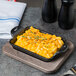A Lodge rectangular wood underliner with a pan of macaroni and cheese on top.