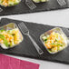 A Visions clear plastic tasting fork on a black slate tray with small bowls of fruit.