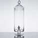 A clear glass Fifth Avenue Crystal beverage dispenser with a black lid and spigot.