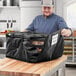 A man in a kitchen holding a black ServIt insulated deli tray bag.