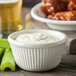 A white Carlisle fluted ramekin filled with dip and surrounded by celery sticks and chicken wings.