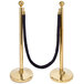 A black rope with brass ends attached to a gold stanchion pole.