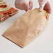A person in gloves putting a sandwich in a Choice brown paper bag.