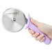 A hand holding a Dexter-Russell purple plastic pizza cutter with a circular blade.