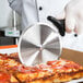 A gloved hand with a black handle cutting a pizza with a Mercer Culinary pizza cutter.