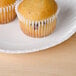A 6" white uncoated paper plate with two muffins on a table.