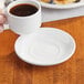 A hand holding a cup of coffee on a white Acopa stoneware saucer.