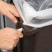A person's hand pulling a plastic bag into a Rubbermaid Slim Jim trash can.