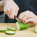 A person using a Dexter-Russell V-Lo scalloped edge paring knife to cut a cucumber.