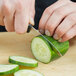 A person using a Dexter-Russell V-Lo scalloped edge paring knife to cut a cucumber.