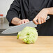 A person using a Dexter-Russell V-Lo chef knife to cut up a head of lettuce on a counter.
