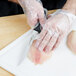 A person in plastic gloves using a Dexter-Russell V-Lo fillet knife to cut fish on a white cutting board.