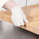 A person wearing gloves and cutting on a Choice wooden cutting board.