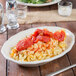 A Tuxton eggshell white china platter with pasta and tomatoes on it.