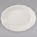A white Tuxton oval china platter with a scalloped edge on a gray surface.