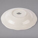 A white Tuxton china bowl with a scalloped edge on a gray surface.