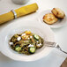 A Tuxton eggshell white china bowl filled with pasta and vegetables with a fork on a table.
