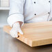 A person in a white coat and gloves using a Choice wood cutting board.